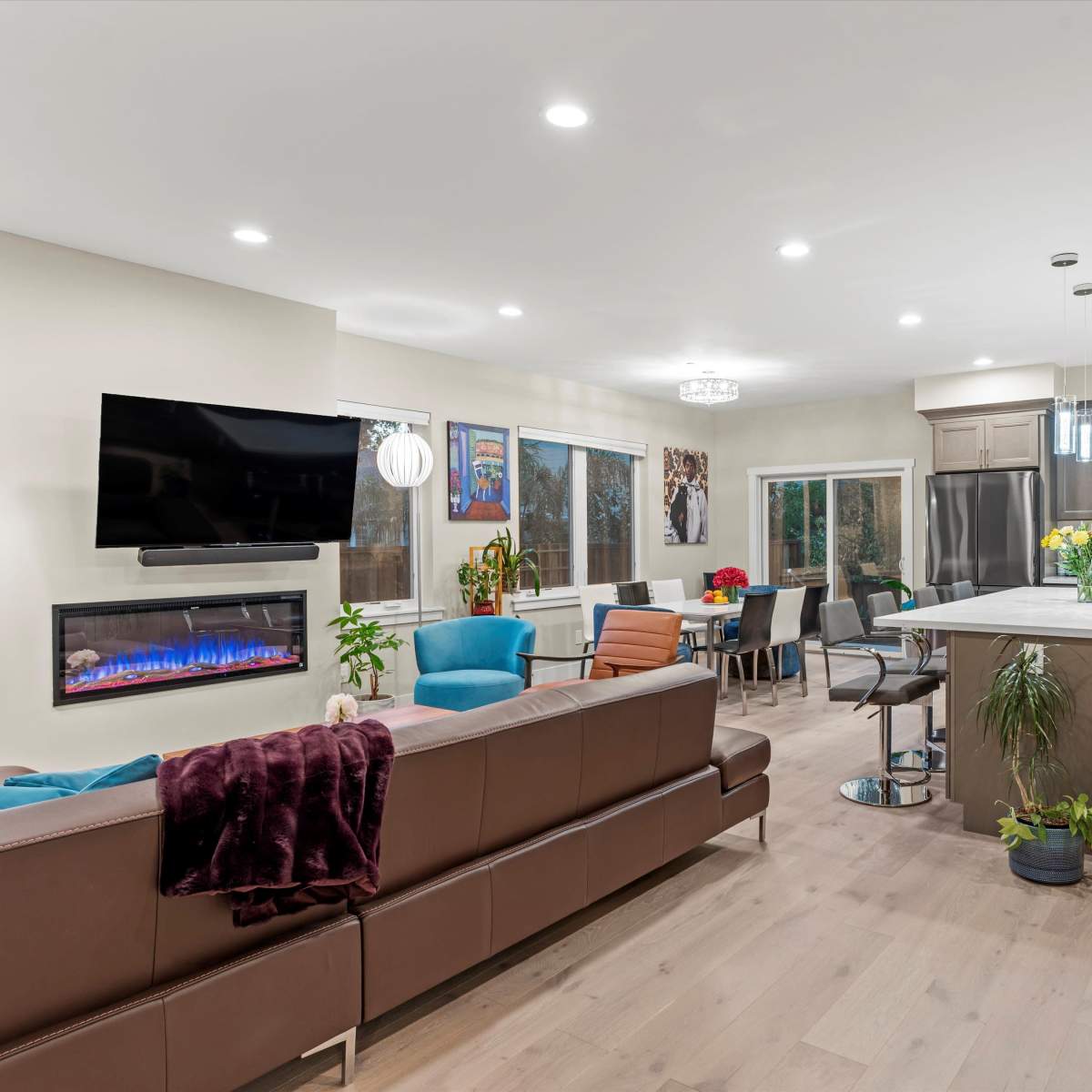 A modern open-concept living space features a kitchen, dining area, and seating lounge with large windows and a mounted television.