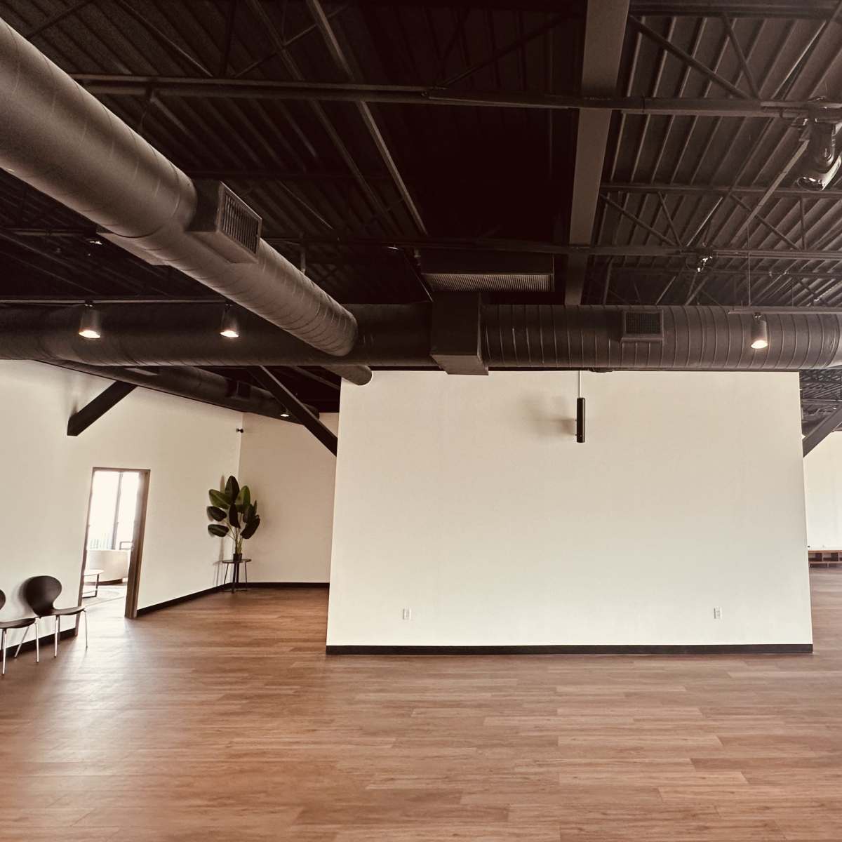 A spacious, empty room with dark beams and ductwork on the ceiling, wooden flooring, and large walls ready for decoration.