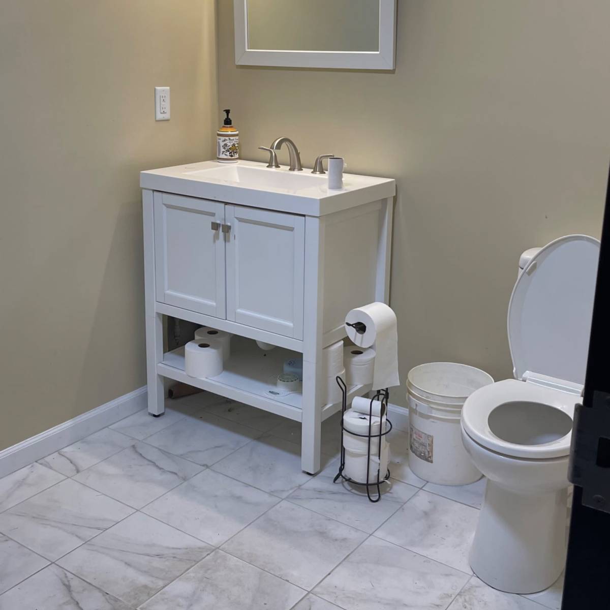 A small bathroom featuring a white vanity with a sink, a mirror above it, a toilet, and tiled flooring.