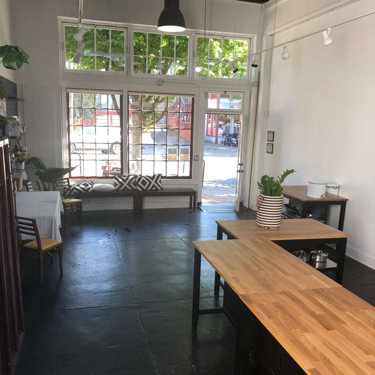 A spacious interior of a café with wooden tables, a white wall, and large windows overlooking a street.