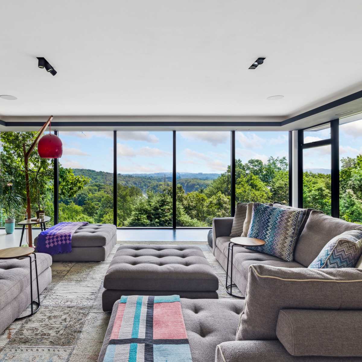 A modern living room features large windows with expansive views of green hills, showcasing comfortable gray sofas adorned with patterned cushions and a cozy throw.