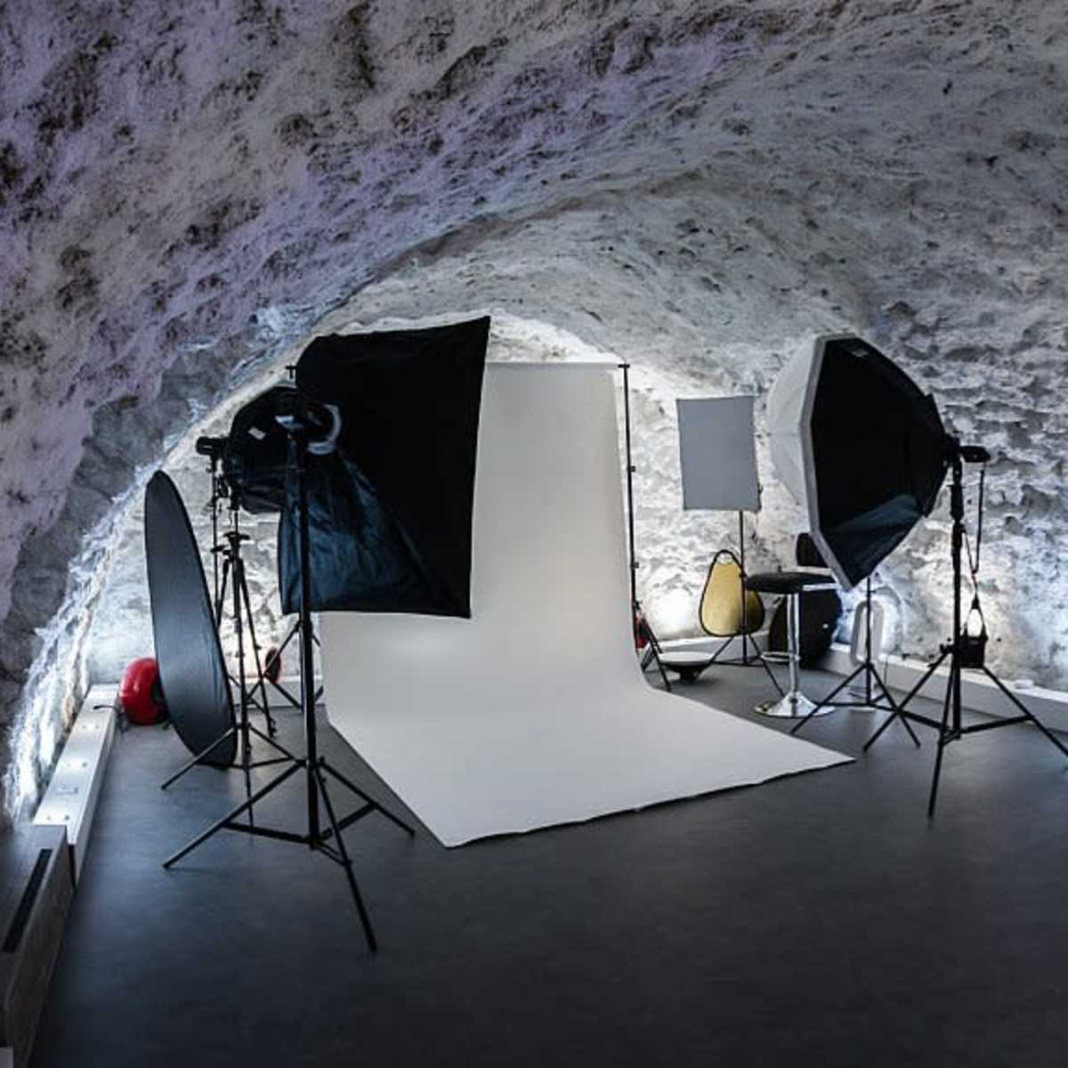 A photography studio with a white backdrop, lighting equipment, and various props in a stone-walled room.
