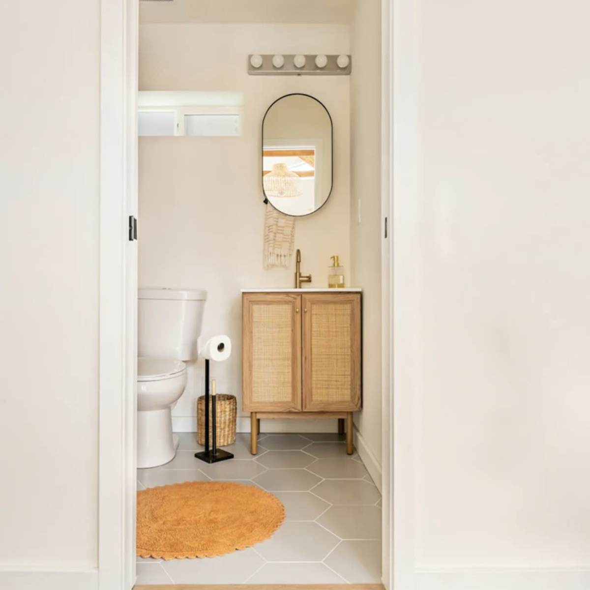 A bathroom doorway with a wooden cabinet, a round mirror, and a toilet, alongside a brown circular rug on the floor.
