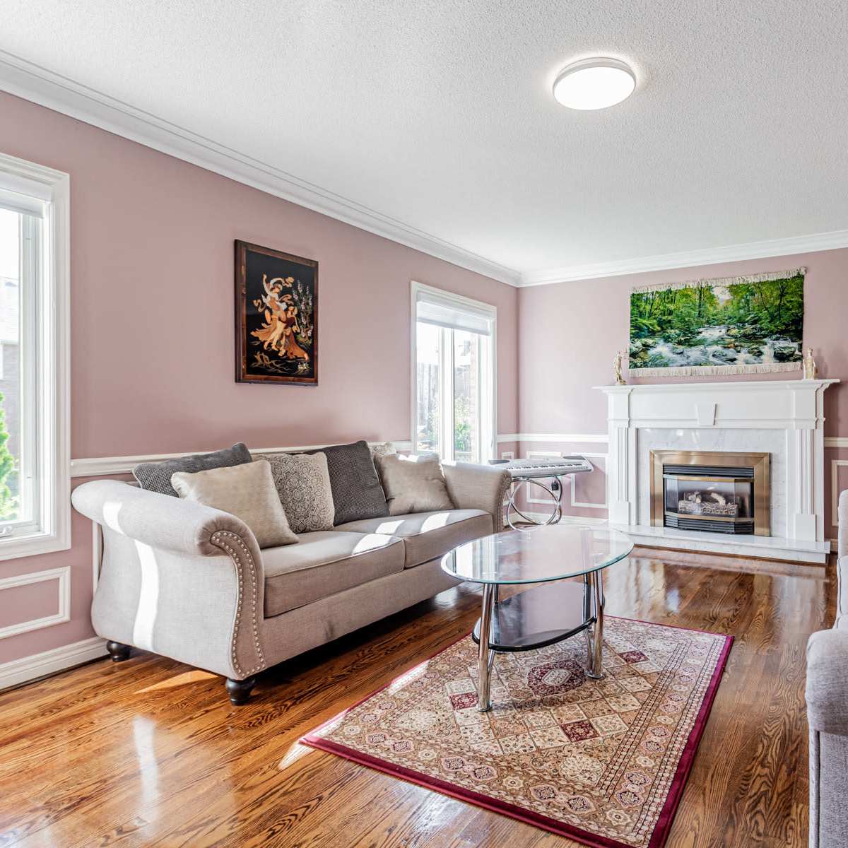 A well-furnished living room with a fireplace and large windows, featuring a light purple wall color and wooden flooring.
