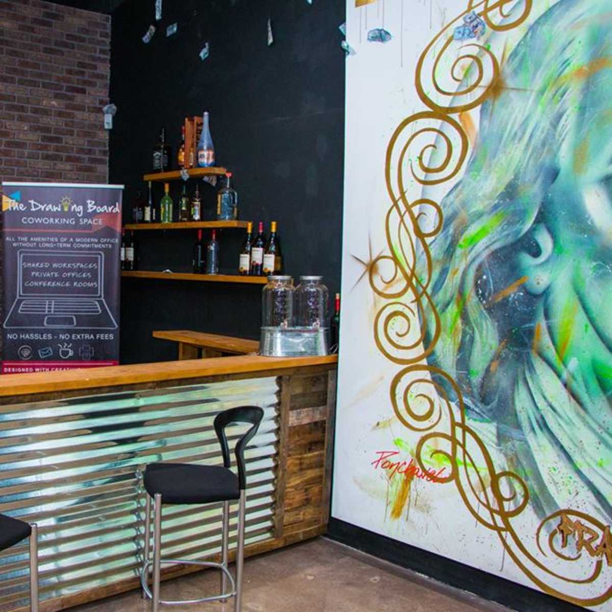 A rustic bar area with a wooden counter, metal accents, and a wall featuring colorful artwork.