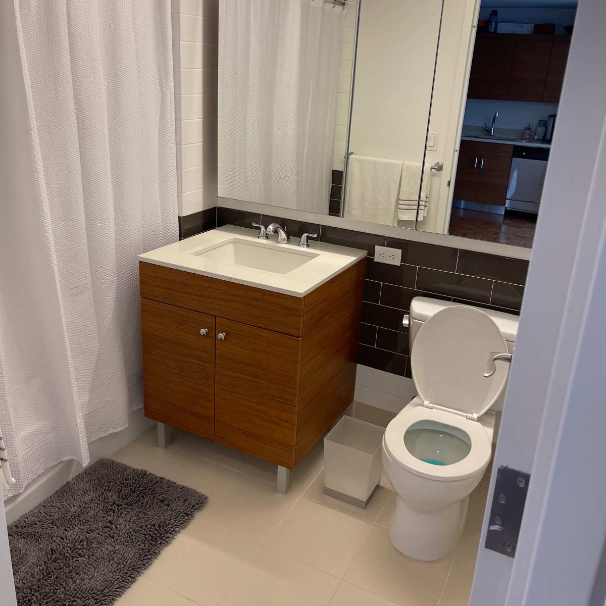A modern bathroom with a shower area, a wooden vanity with a sink, a toilet, and a mirror.