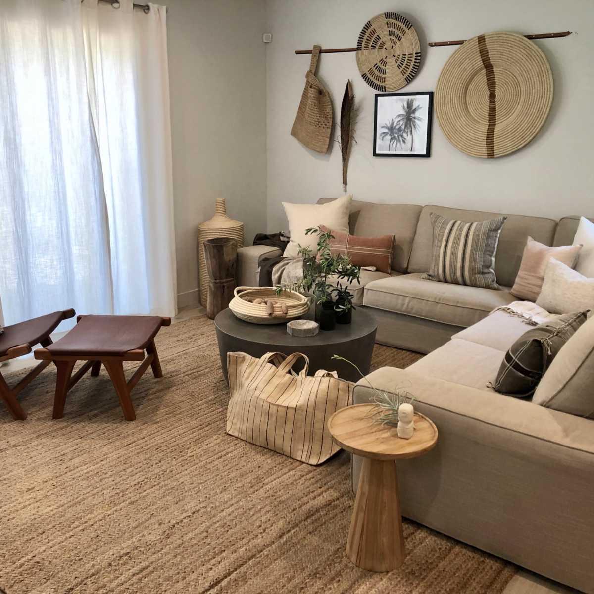 A light, modern living room with a sectional sofa, a coffee table, and a chair, surrounded by natural decor elements and a woven rug.