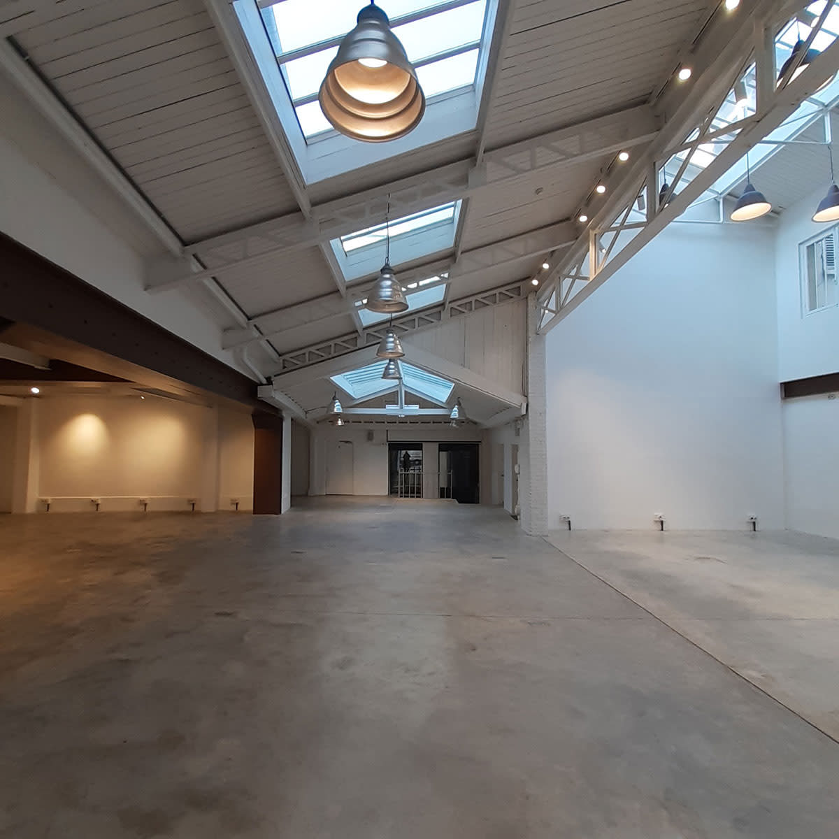 A spacious, empty interior of a building with high ceilings, large windows, and a polished concrete floor.