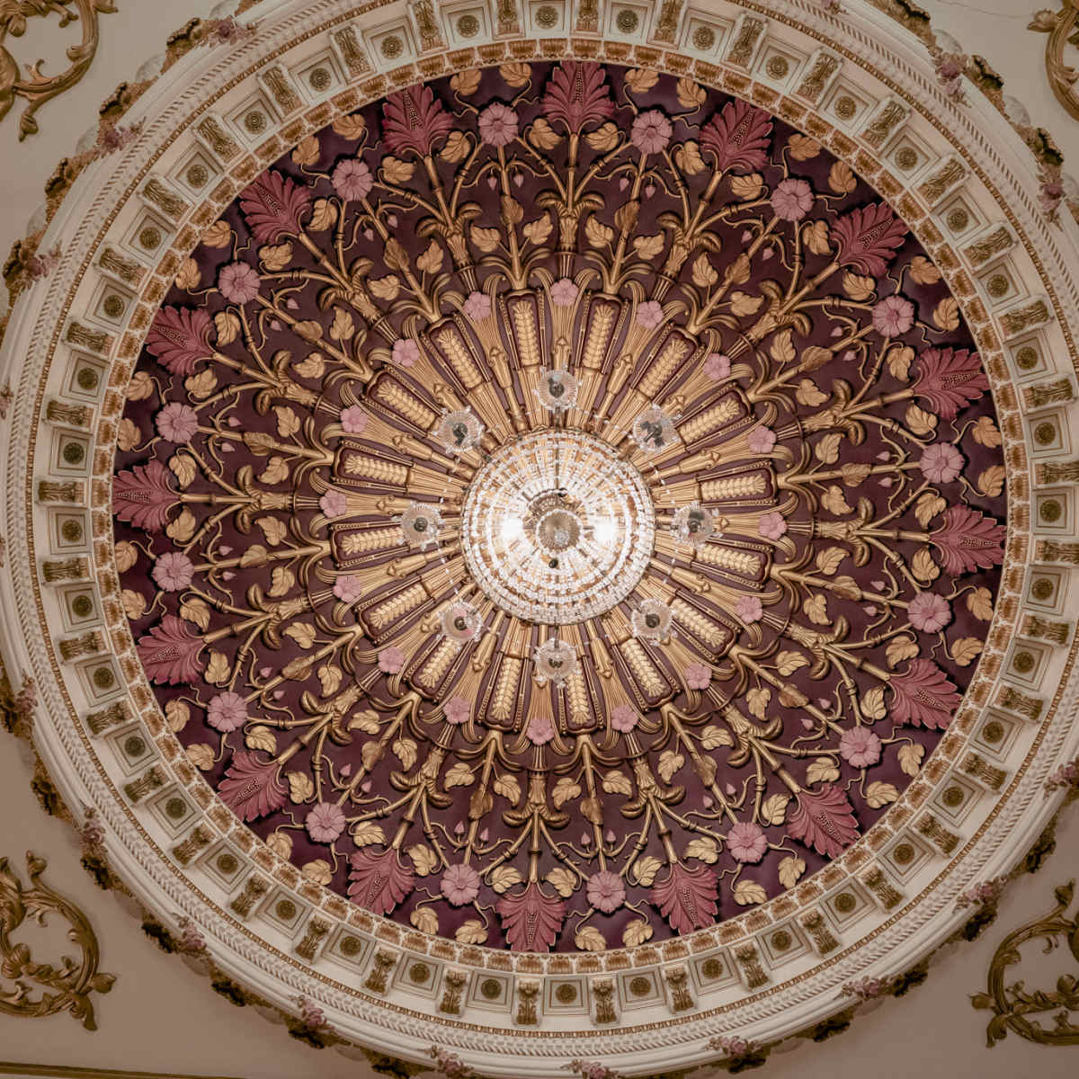 An ornate ceiling featuring a circular design with floral patterns and a central chandelier.