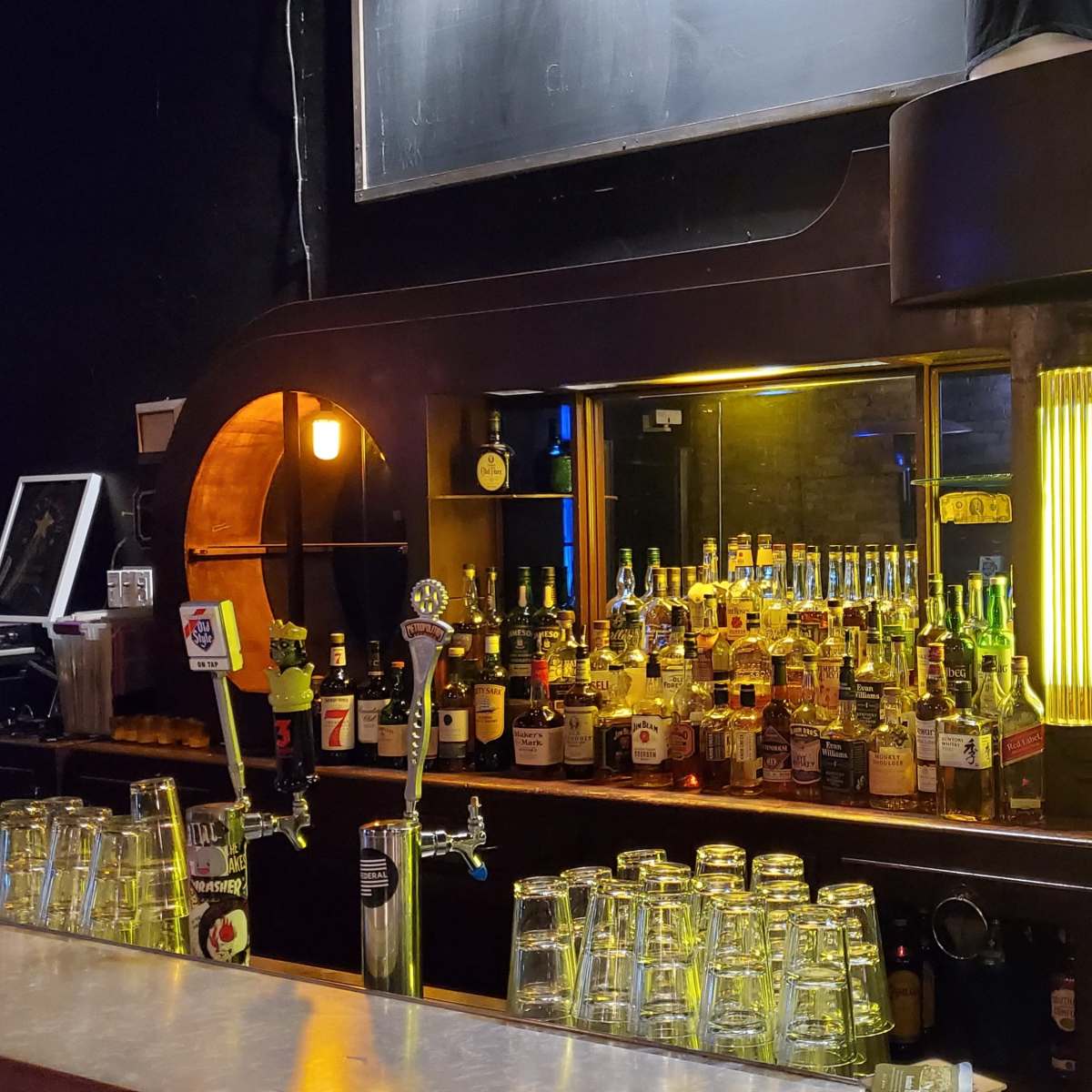 A dimly lit bar with shelves filled with various bottles of liquor and illuminated displays behind the counter.