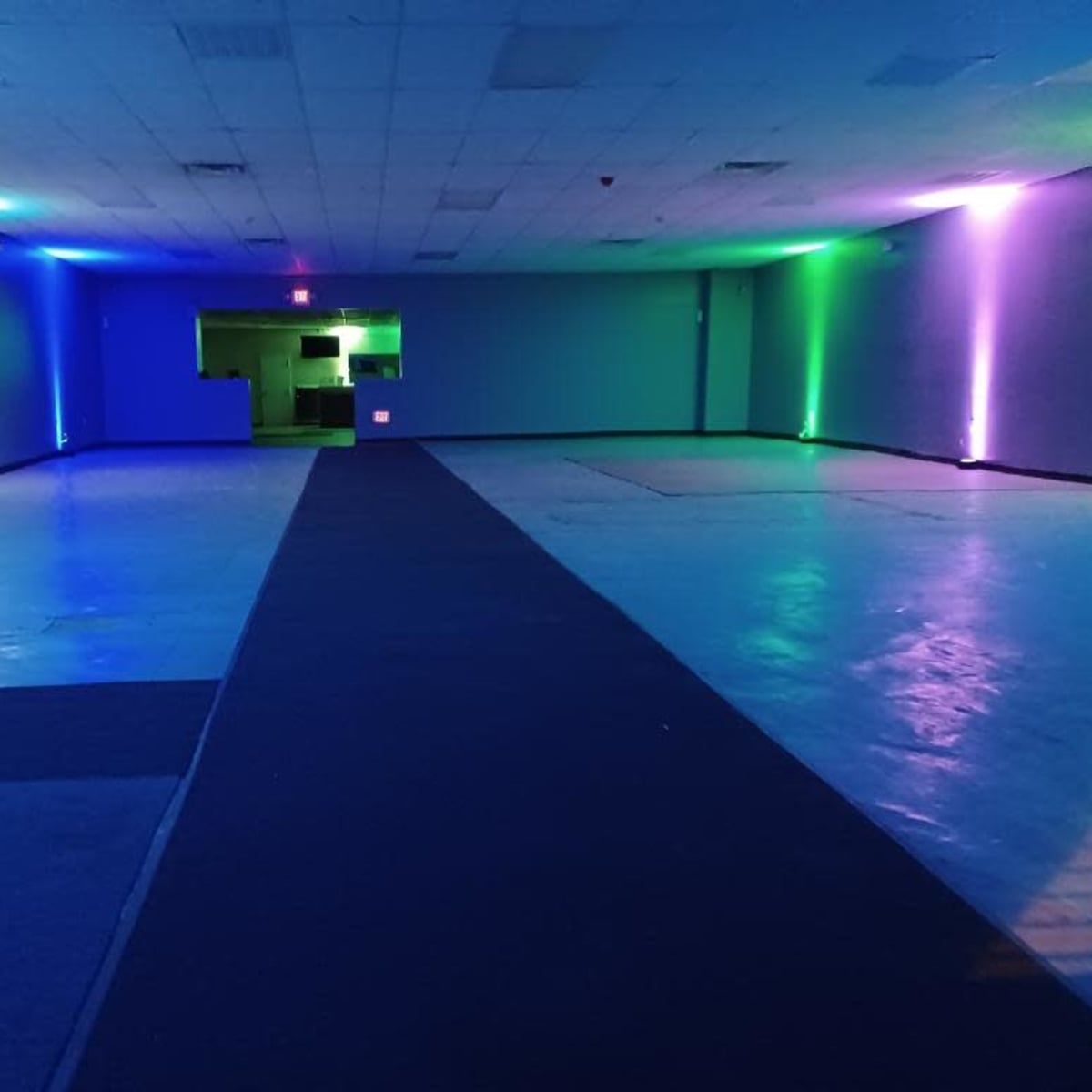 An empty, dimly lit room with blue and green neon lights along the walls and a dark walkway down the center.