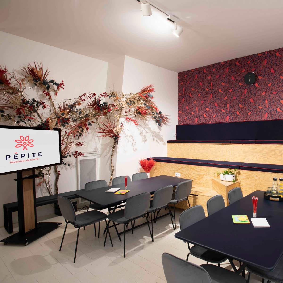 A meeting room with wooden seating, dark tables, and a decorative wall featuring a red floral pattern.