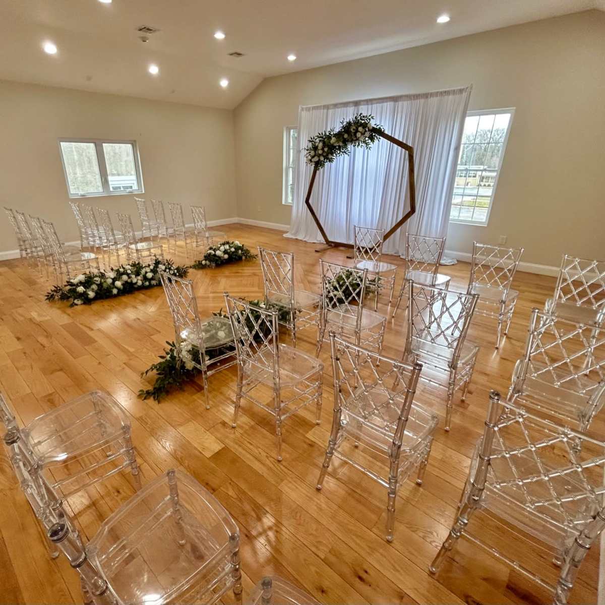 A room is set up for a ceremony, featuring transparent chairs arranged in a circular formation around a decorated altar with floral accents.