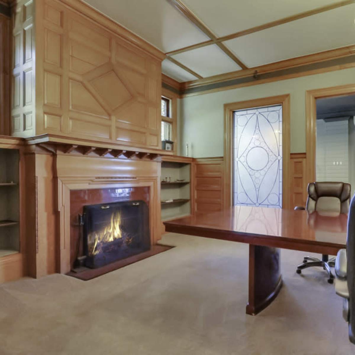 A warmly designed room featuring a wooden fireplace, a large conference table, and decorative glass doors.