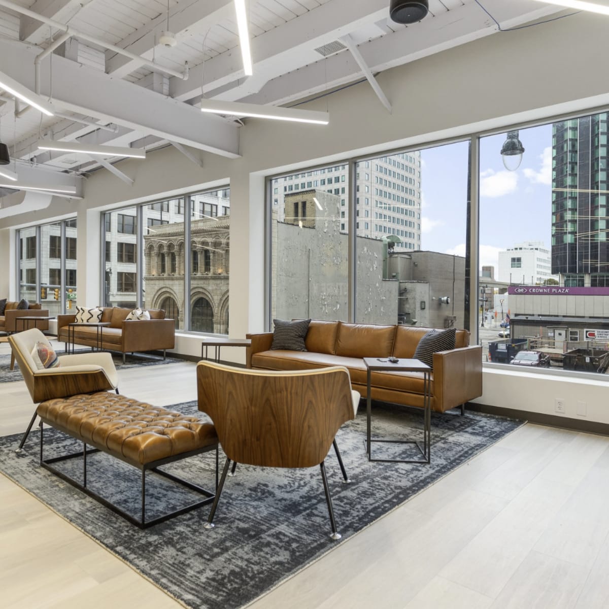 A modern lounge area with leather seating, large windows overlooking a cityscape, and minimalistic decor.
