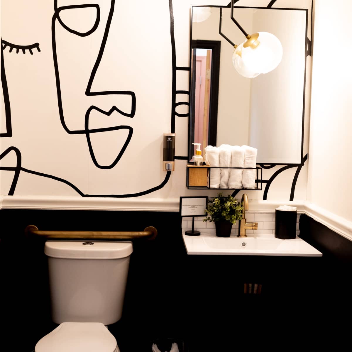 A bathroom with a black and white mural on the wall, a white toilet, a marble countertop with neatly arranged towels, and a decorative mirror.