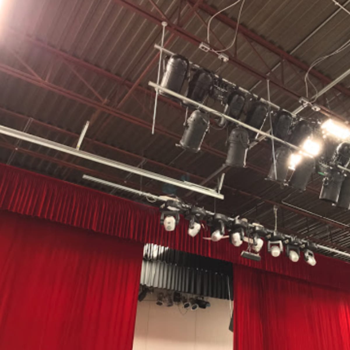 A stage setup with overhead lighting fixtures and red curtains in a performance space.