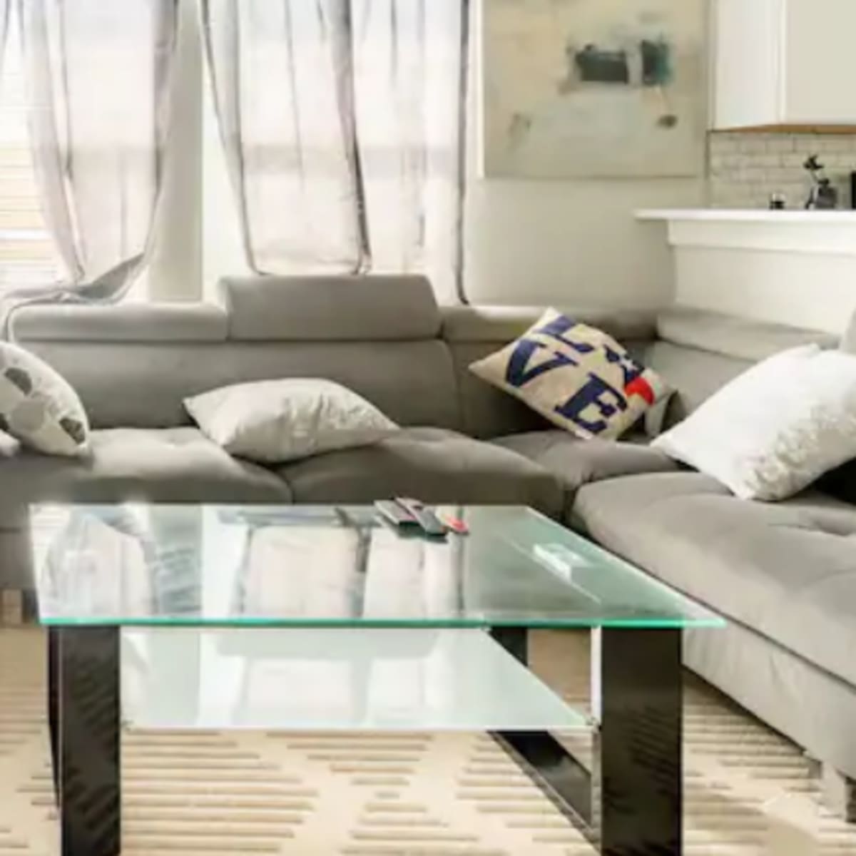 A modern living room featuring a sectional sofa, a glass coffee table, a hanging chair, and large windows with sheer curtains.