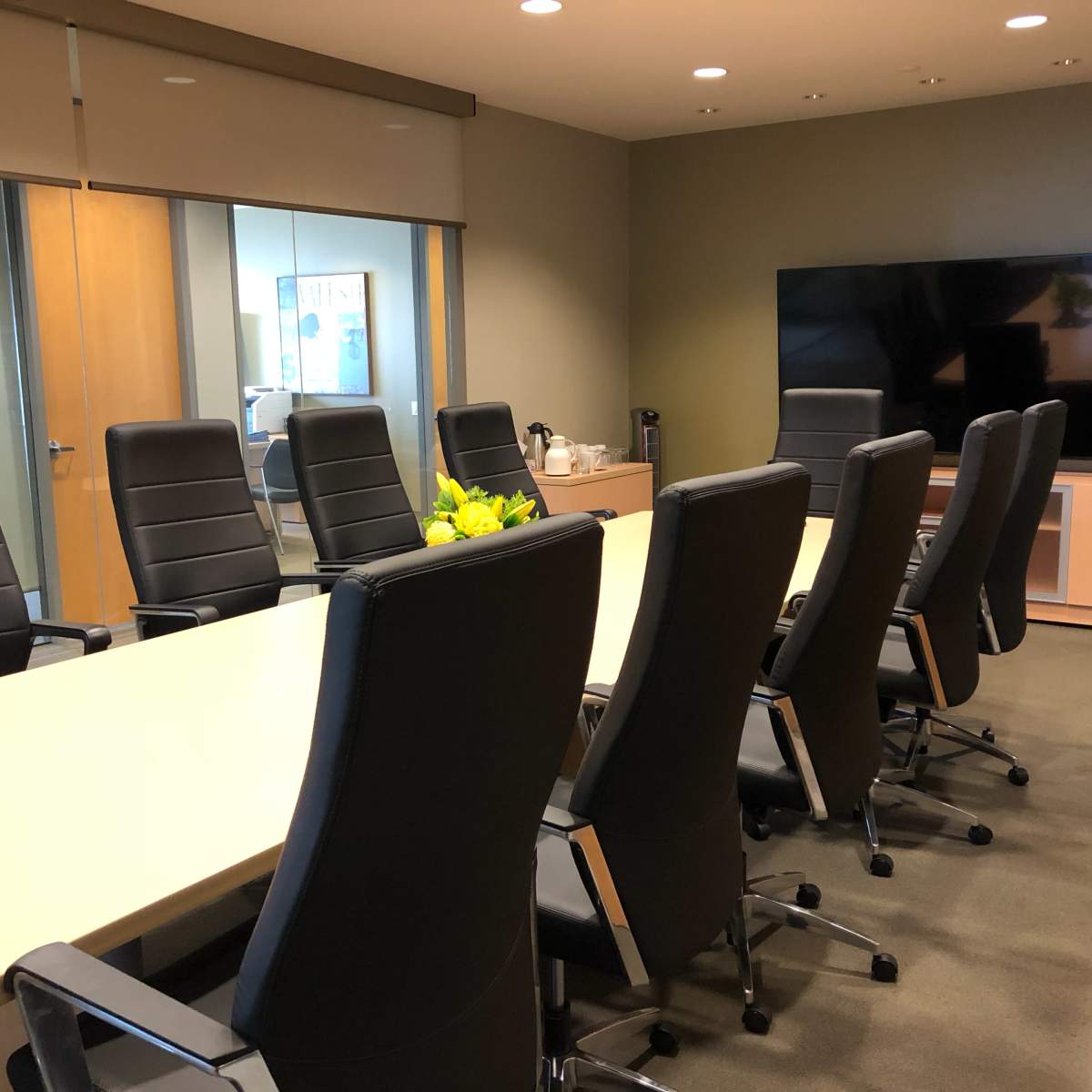 A modern conference room is set with a long table surrounded by high-backed black chairs and features a large screen on one wall.