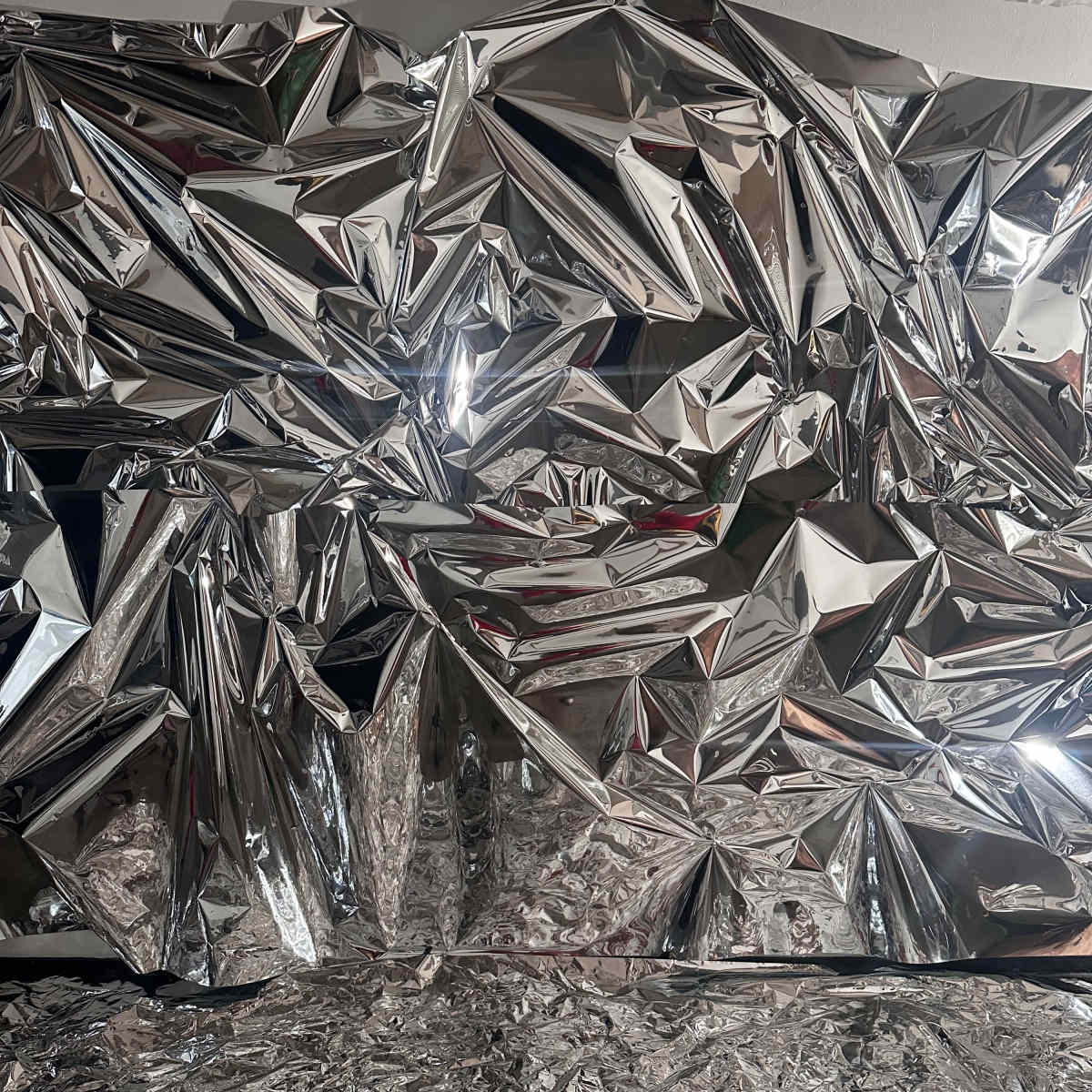 A crumpled and shiny metallic foil surface, reflecting light and creating a textured appearance.