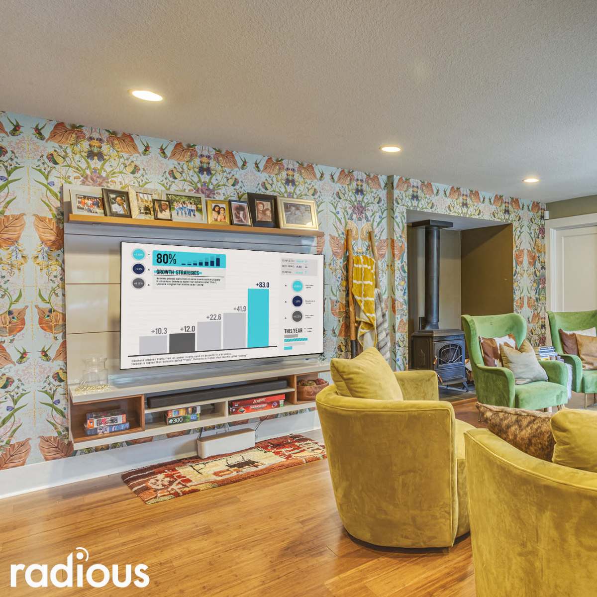 A cozy living room features green chairs, a television displaying a data visualization, and a floral-patterned wall.
