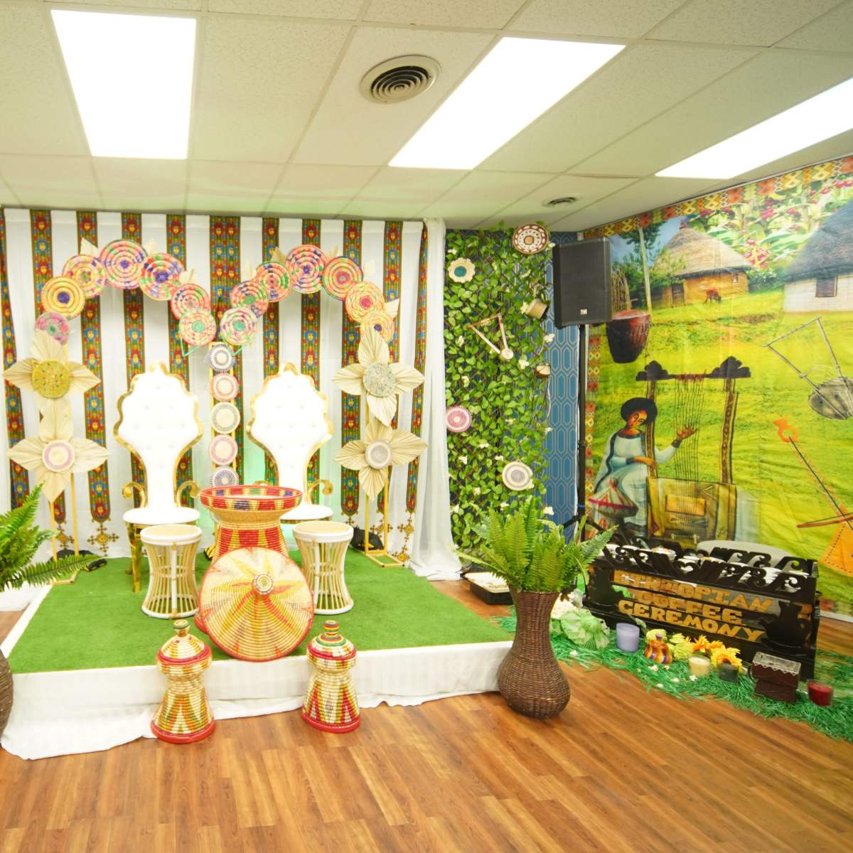 A decorated indoor space with colorful circular decorations, greenery on the walls, and two chairs set on a turf-like surface, flanked by potted plants.