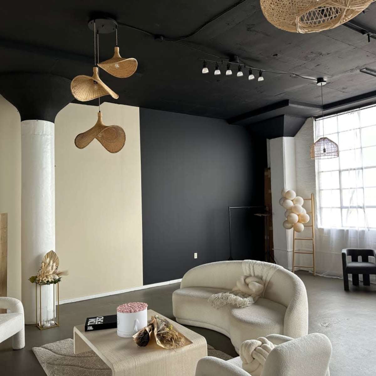 A modern interior space with beige and dark walls, featuring circular seating arrangements, decorative elements, and large windows allowing natural light.