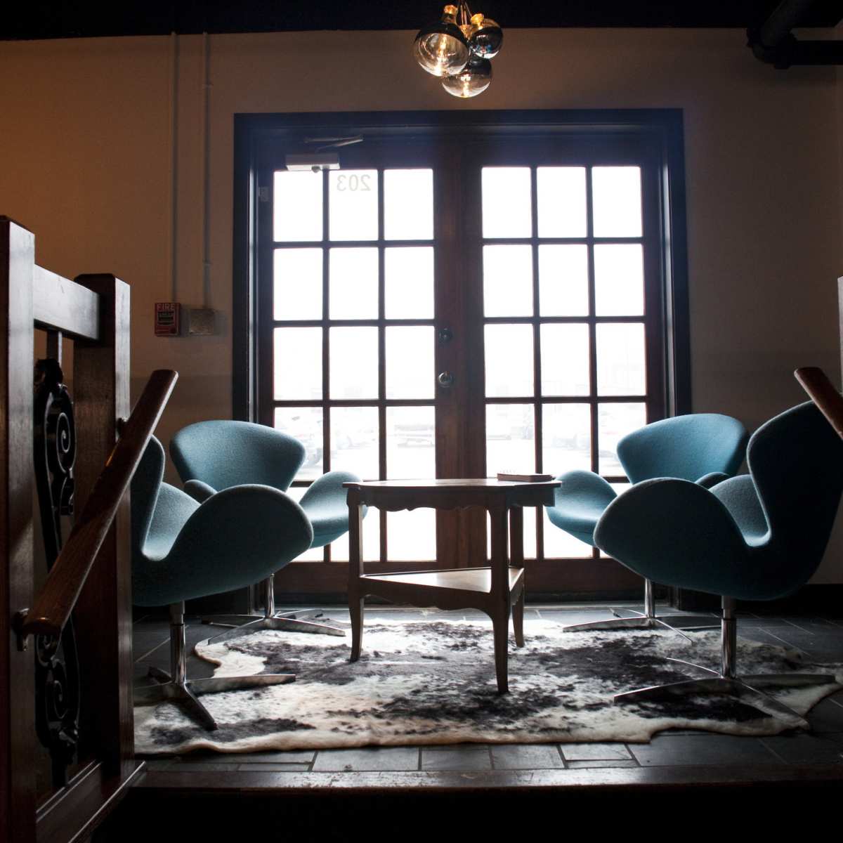A cozy seating area features four blue chairs arranged around a wooden table on a cowhide rug, with large windows providing natural light.