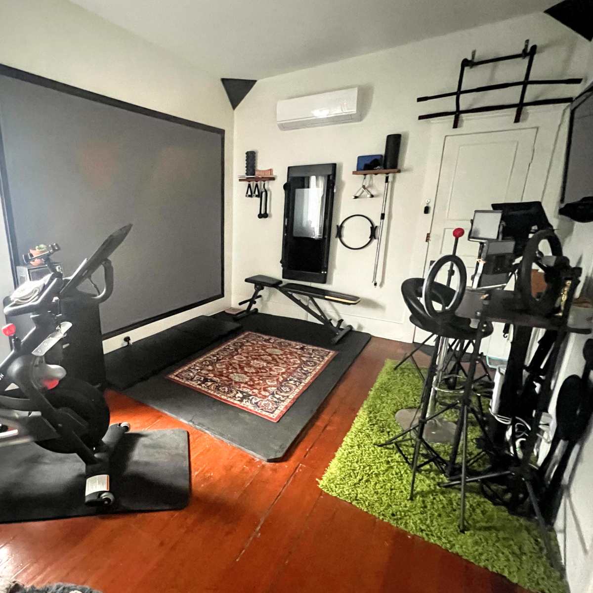 A home gym with exercise equipment, including a stationary bike, weights bench, and fitness accessories arranged around a center rug.