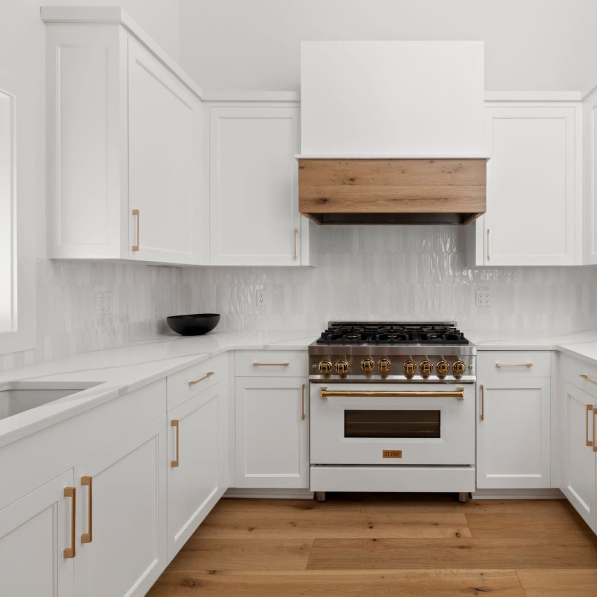 A modern kitchen features white cabinets, a wooden range hood, and a stainless steel stove.