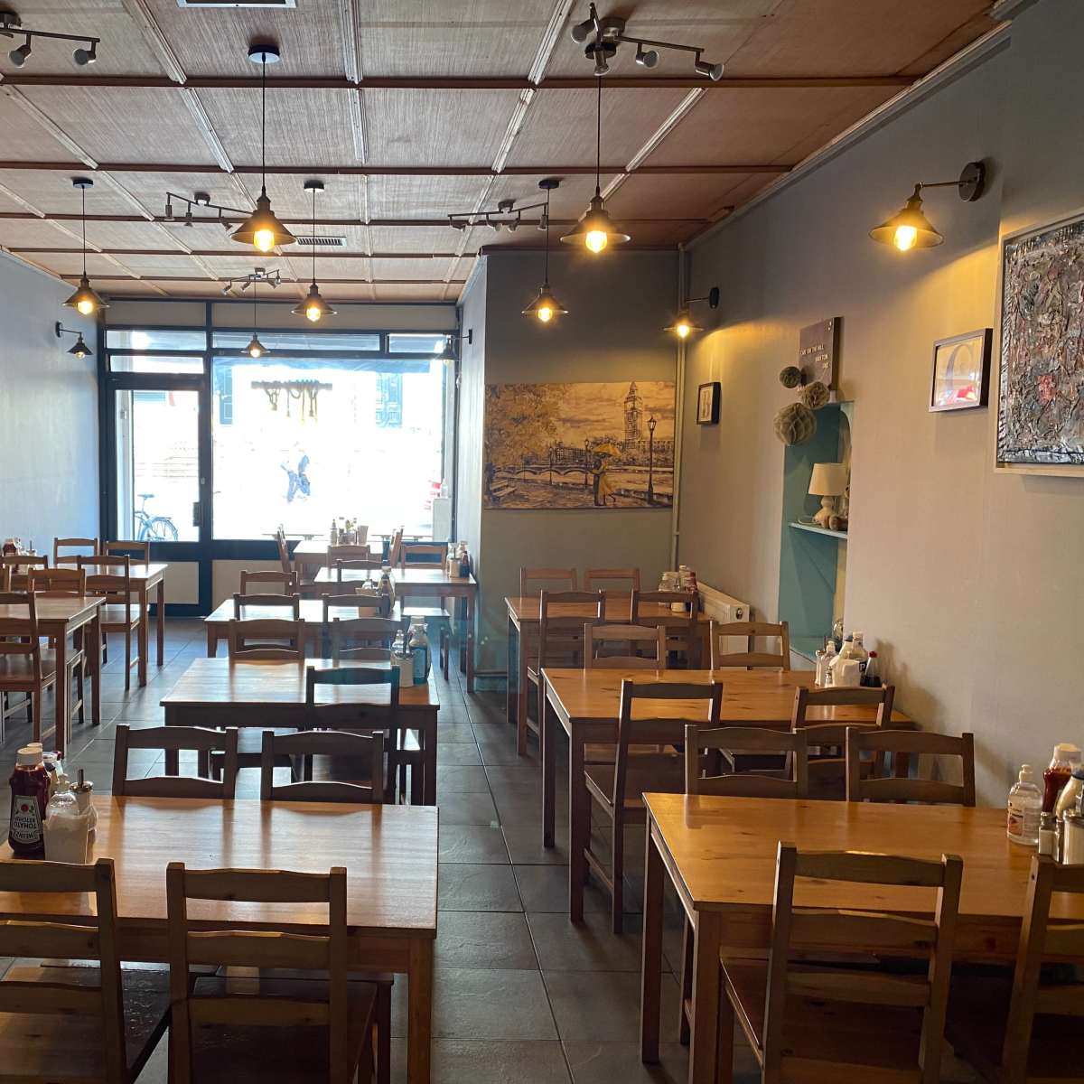 An empty restaurant interior with wooden tables and chairs, and warm lighting.