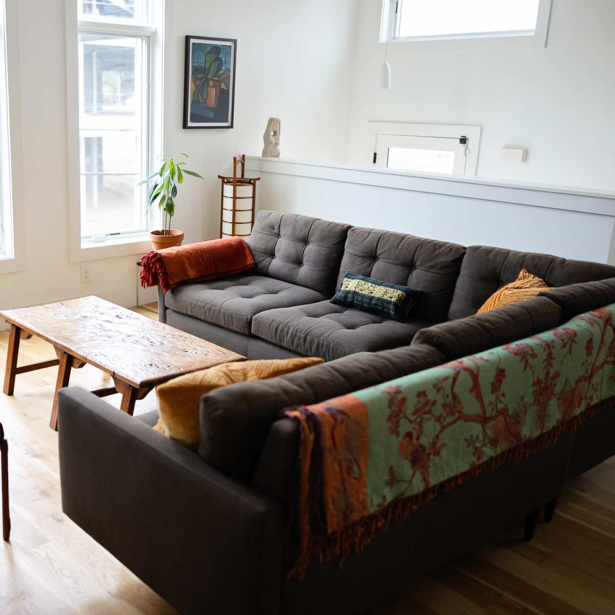 A modern living room with a gray sofa, two chairs, a wooden coffee table, and large windows allowing natural light.
