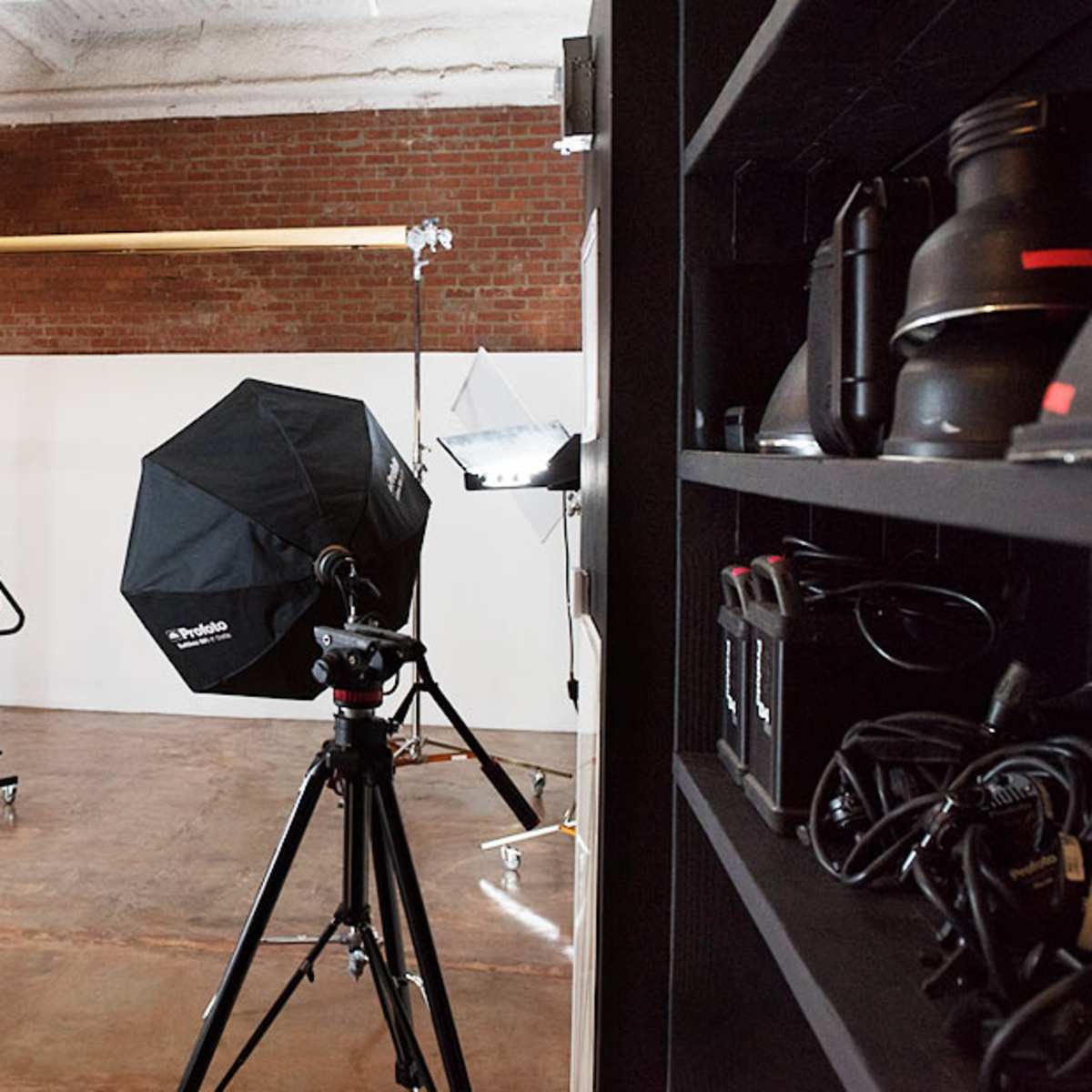 A photography studio equipped with various lighting setups, a backdrop support, and camera equipment on a shelf.