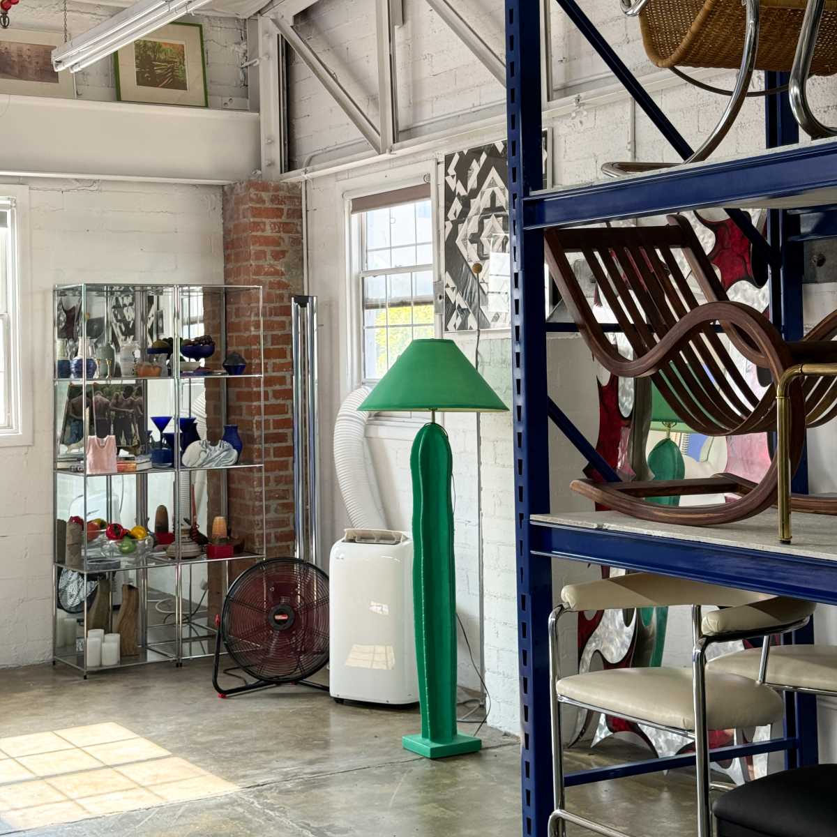 A modern interior space featuring shelves with various chairs, a green lamp, and a mirrored display cabinet filled with decorative items.