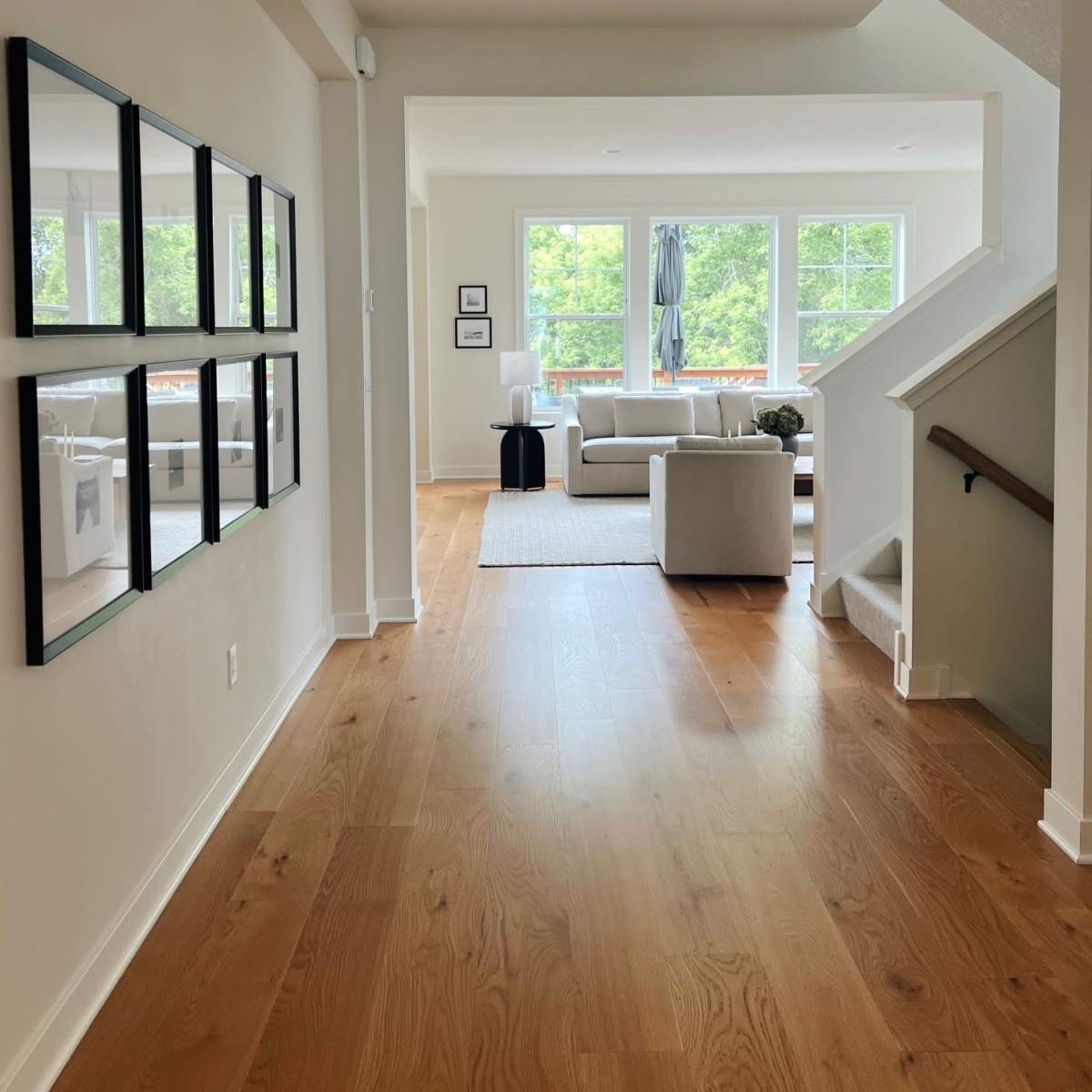 A hallway leads to a bright living room with large windows and a staircase on the right.