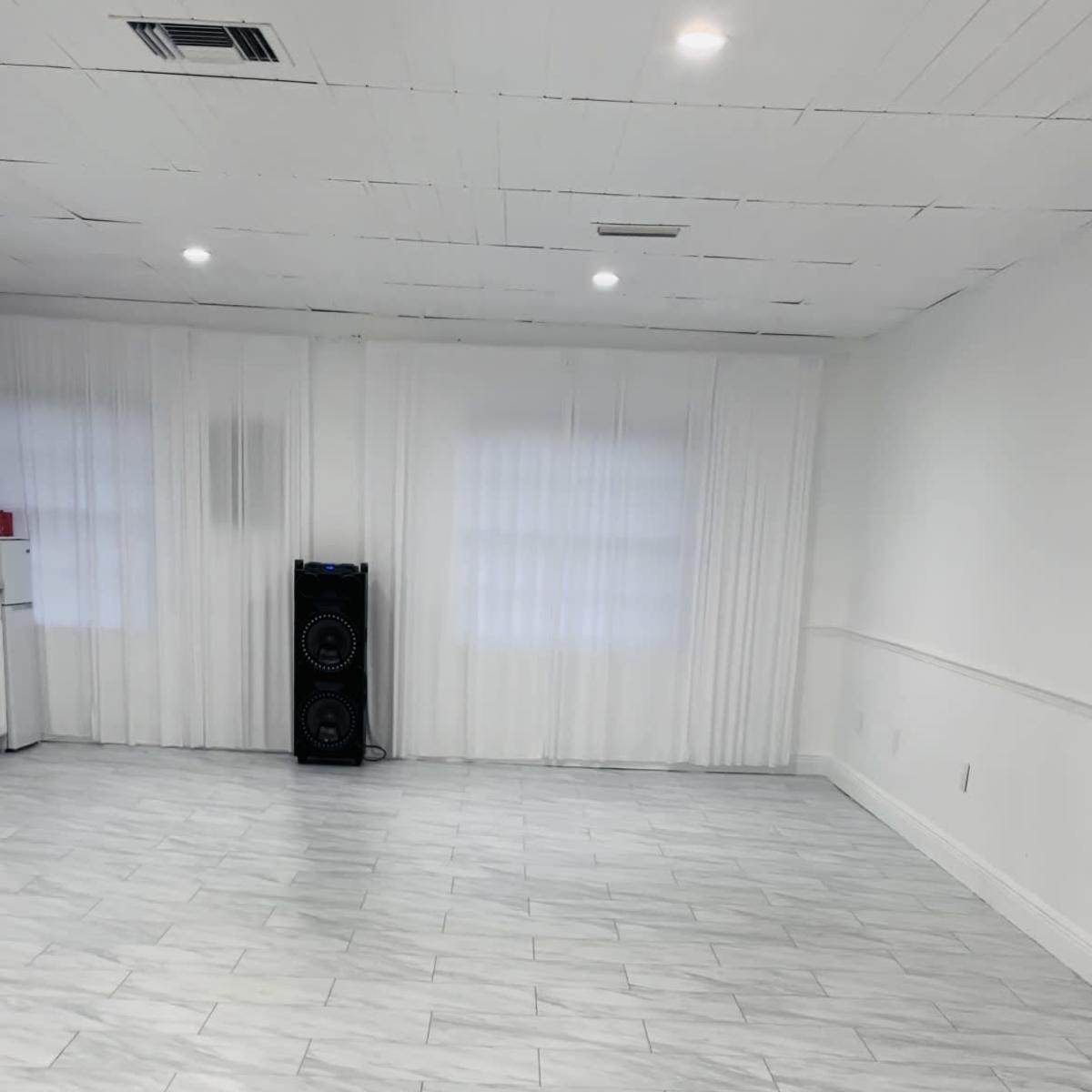 A spacious interior room with white marble tile flooring and large windows covered by sheer curtains.