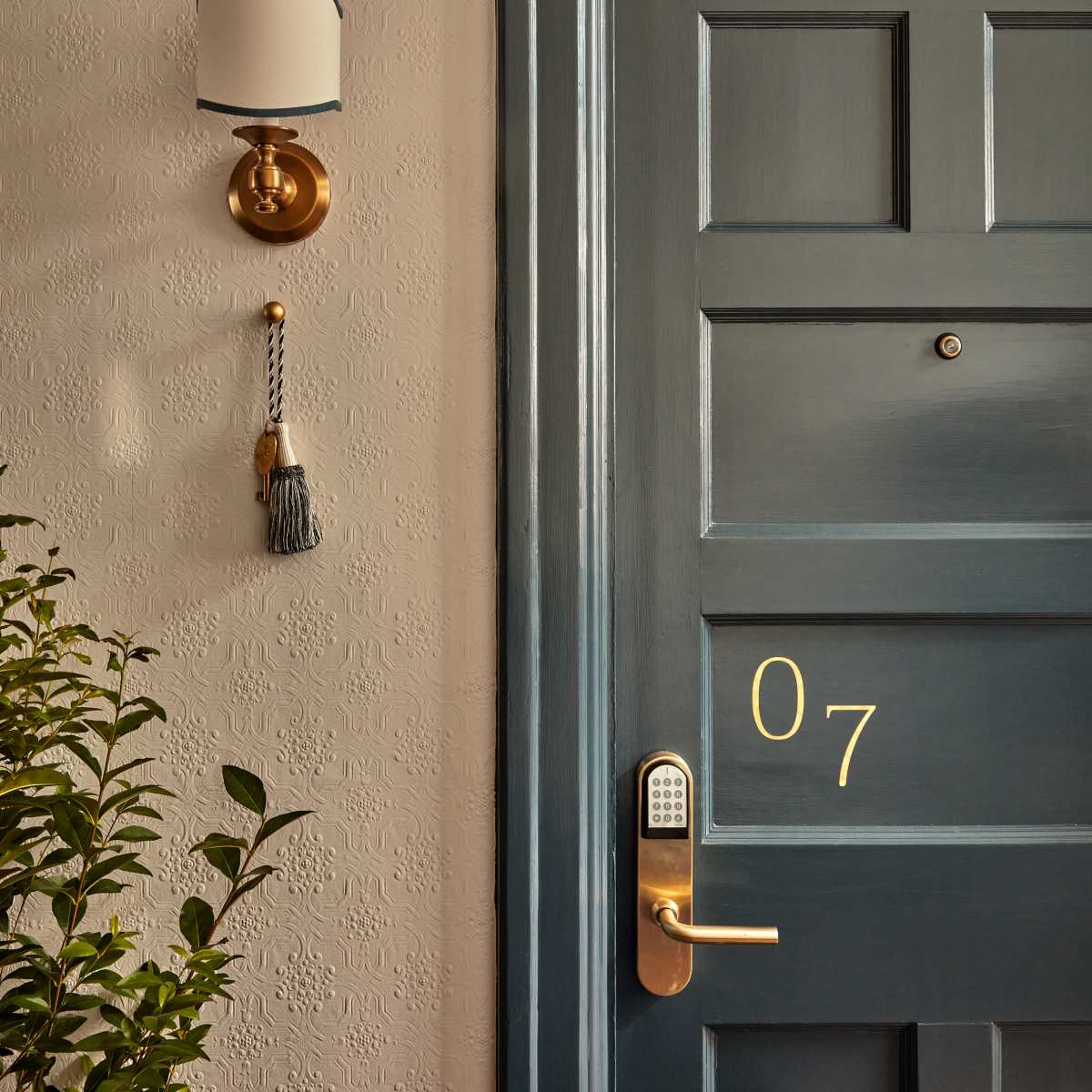 A blue door with the number 07, a wall-mounted sconce, and a decorative tassel beside it.