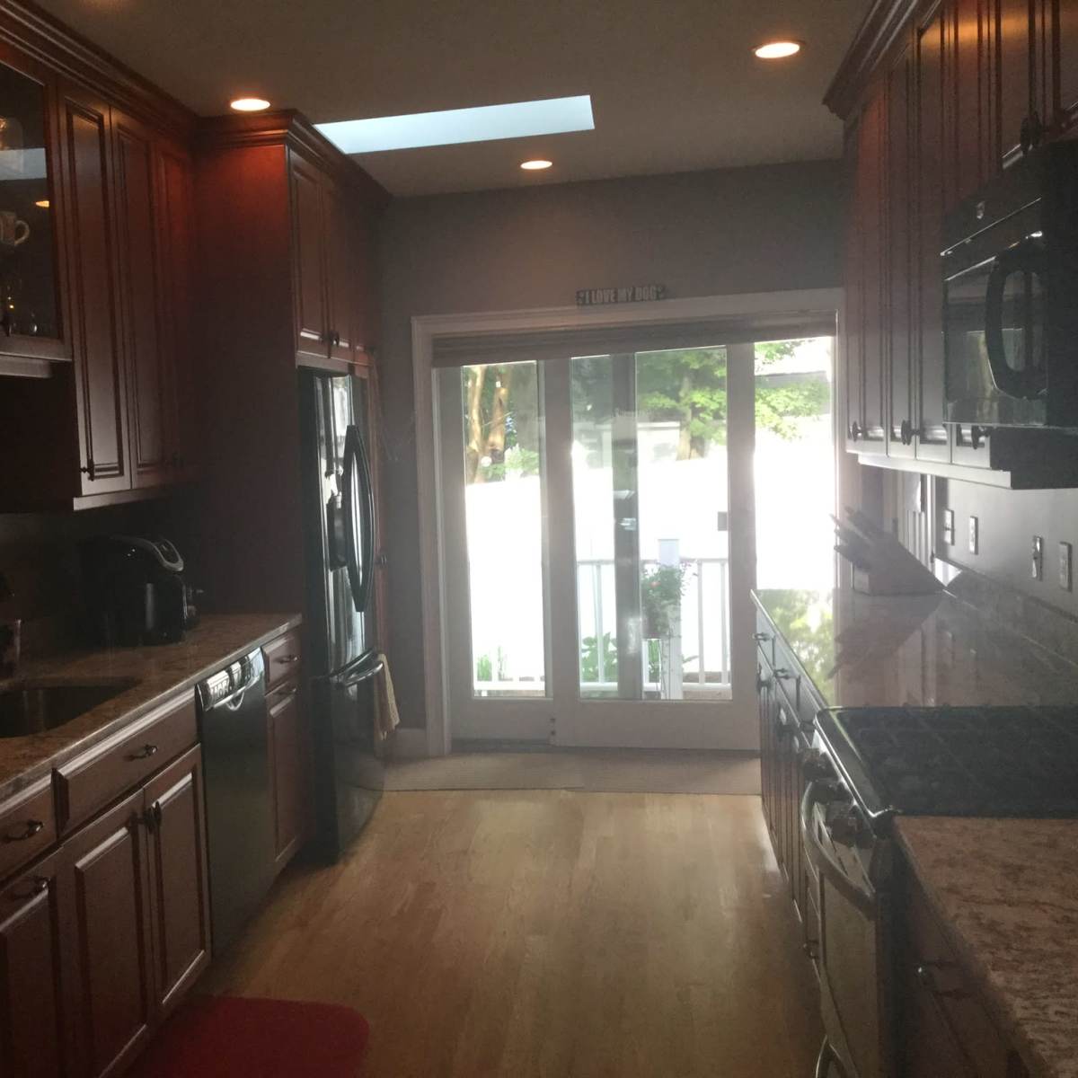 A modern kitchen with wooden cabinets, a stone countertop, and a sliding glass door leading to an outside area.