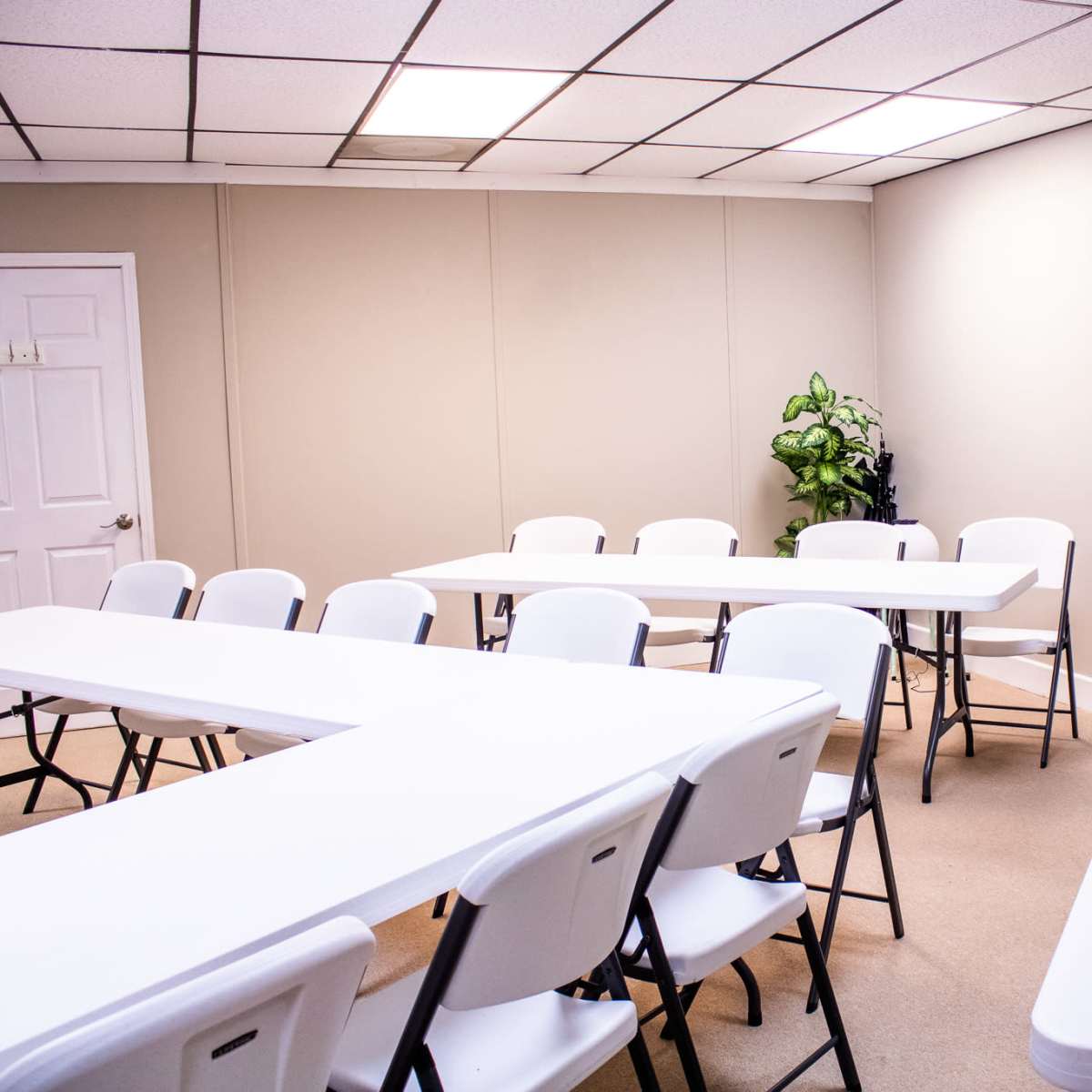 A meeting room with several white tables and chairs arranged around the space, and a television mounted on the wall.
