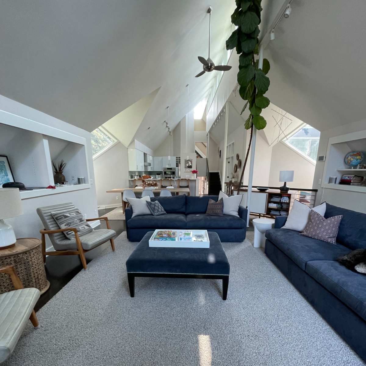 A spacious, modern living room with a blue sofa, a coffee table in the center, and large windows that provide ample natural light.