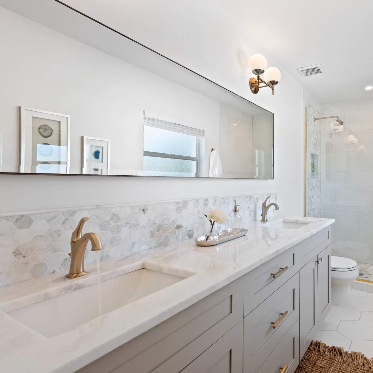A modern bathroom featuring a two-sink vanity with a large mirror, a tiled shower area, and neutral decor elements.