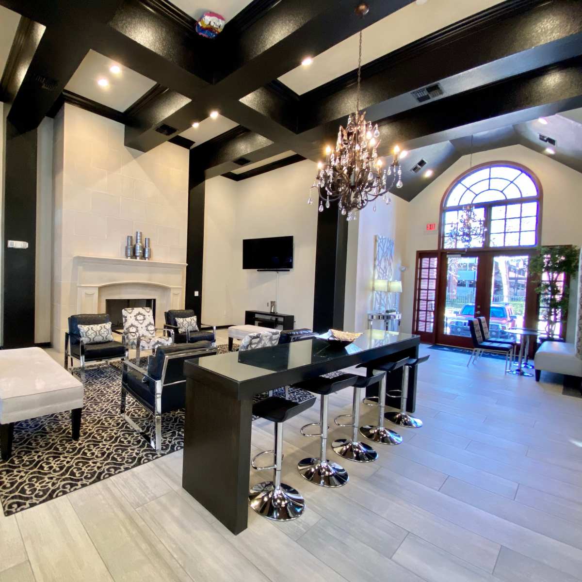 A modern lounge area with dark wooden beams, a fireplace, chic furniture, and a dining space featuring high stools at a long table.
