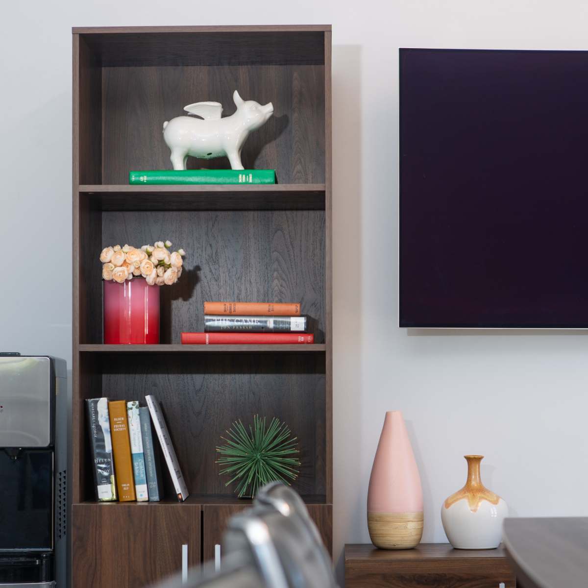 A modern shelving unit displays decorative items and books next to a sleek dining table and a television mounted on the wall.