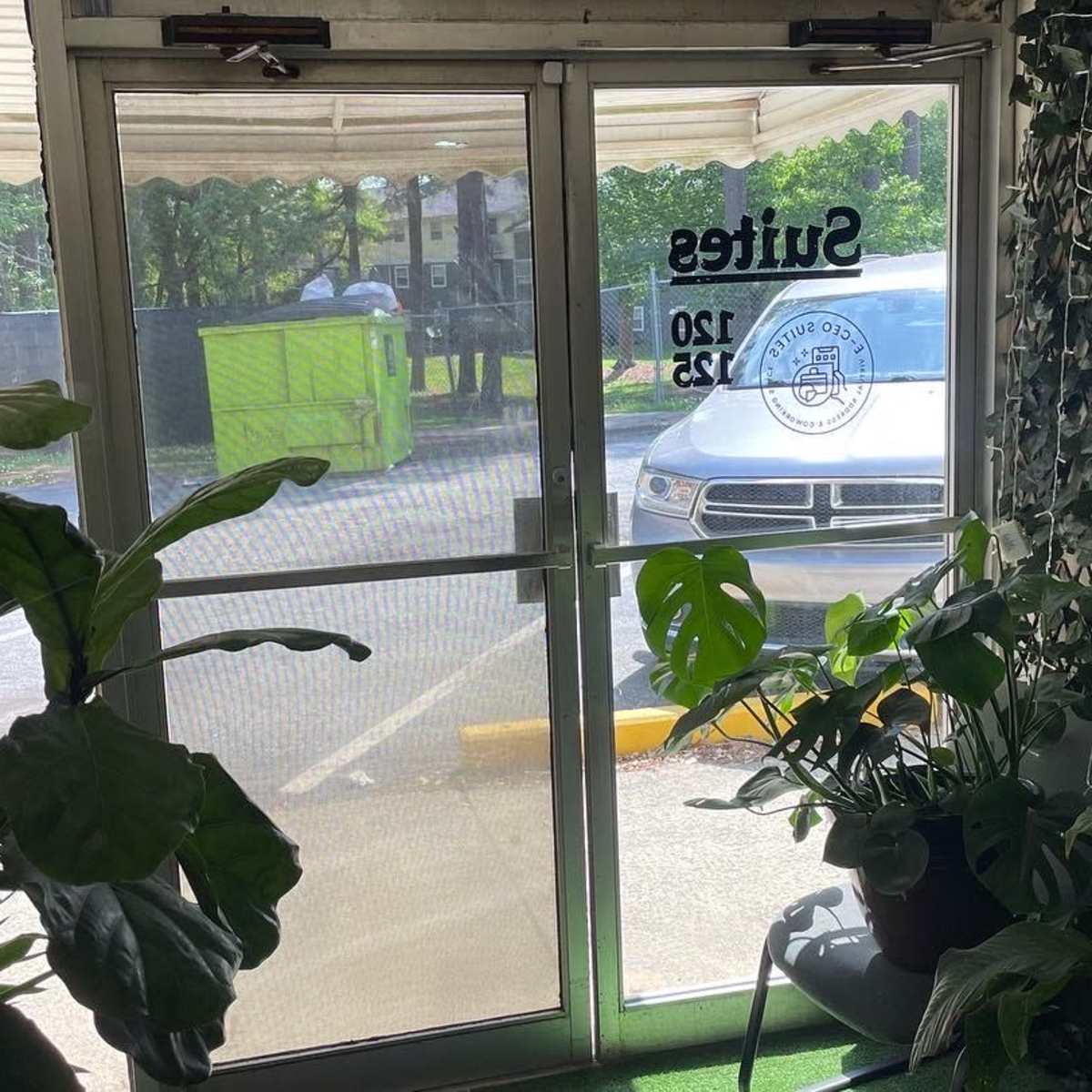A glass entrance door with a leafy wall on one side and a view of a parking lot through the door.