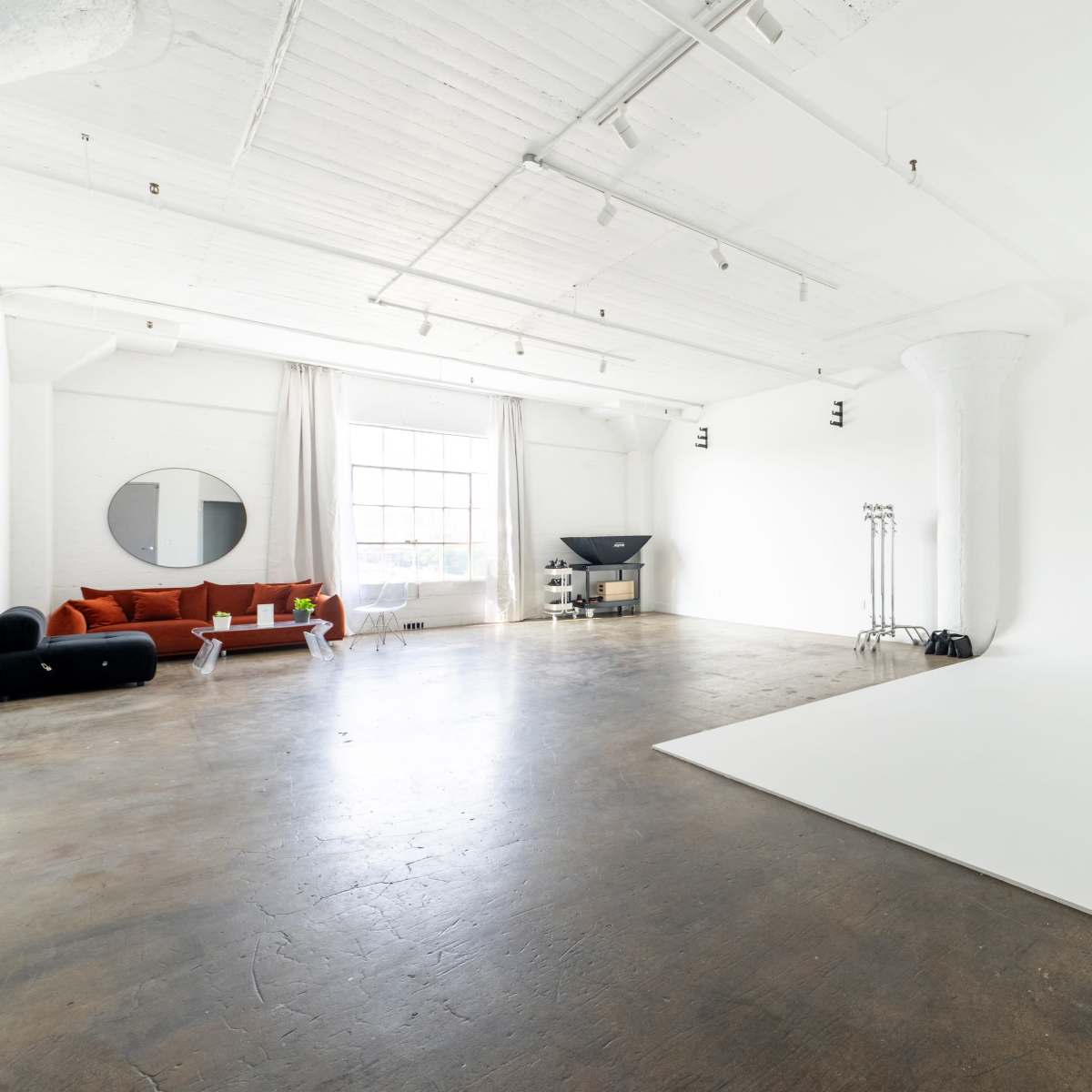 A spacious, modern studio features a white backdrop, polished concrete floor, and minimalist furniture including a red couch.