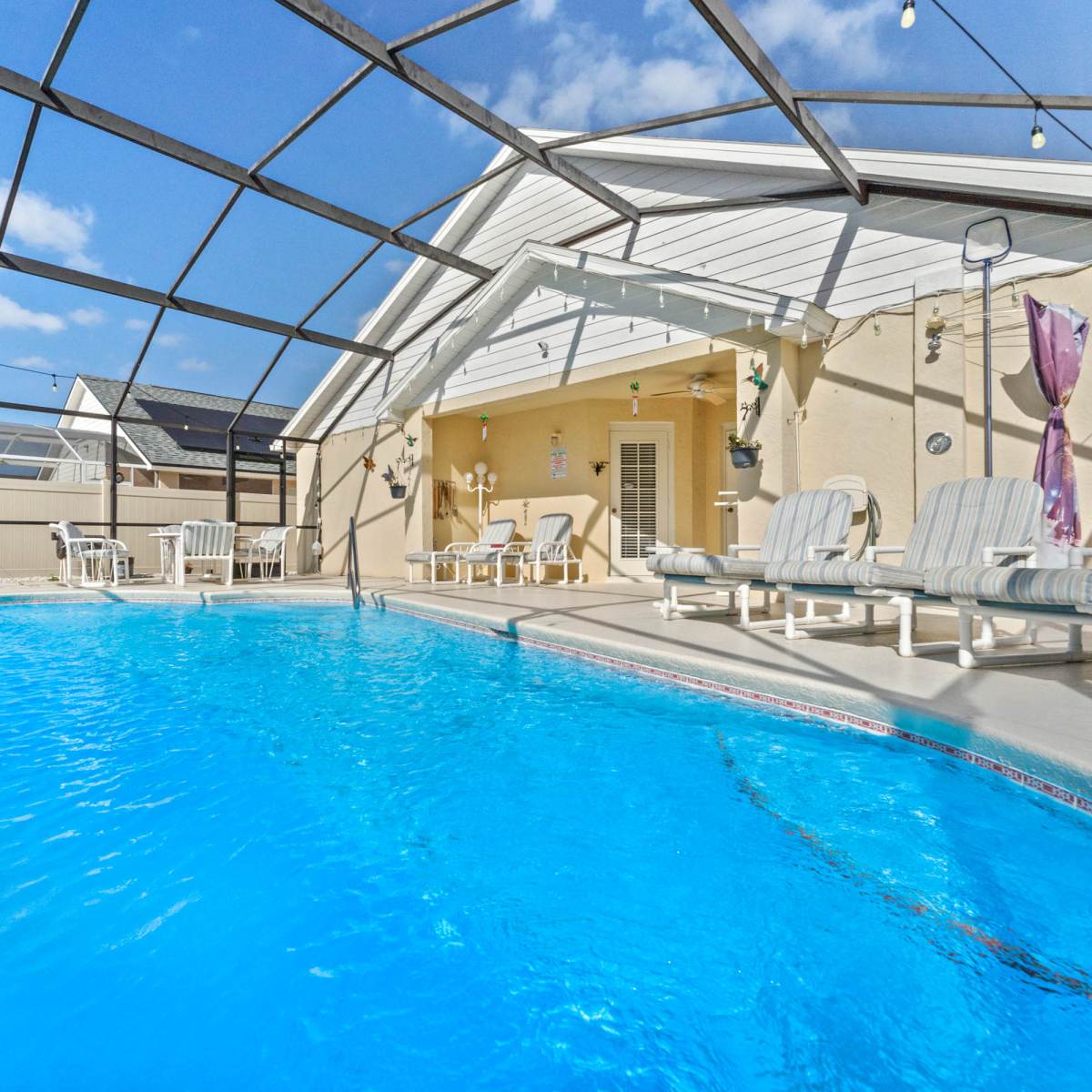 A blue swimming pool enclosed by a metal frame and featuring lounge chairs along the side.