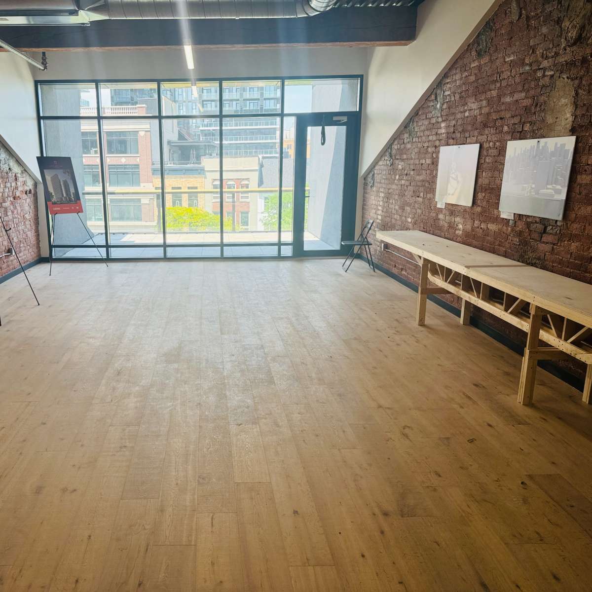 An empty room with brick walls, large windows, and a wooden table along one side.