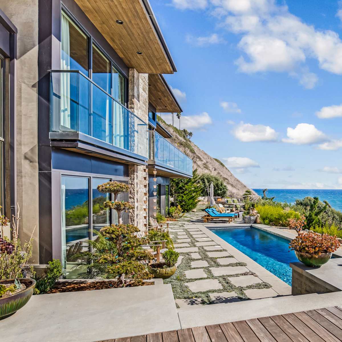 A modern seaside home features a terrace with a pool, landscaped pathways, and ocean views.