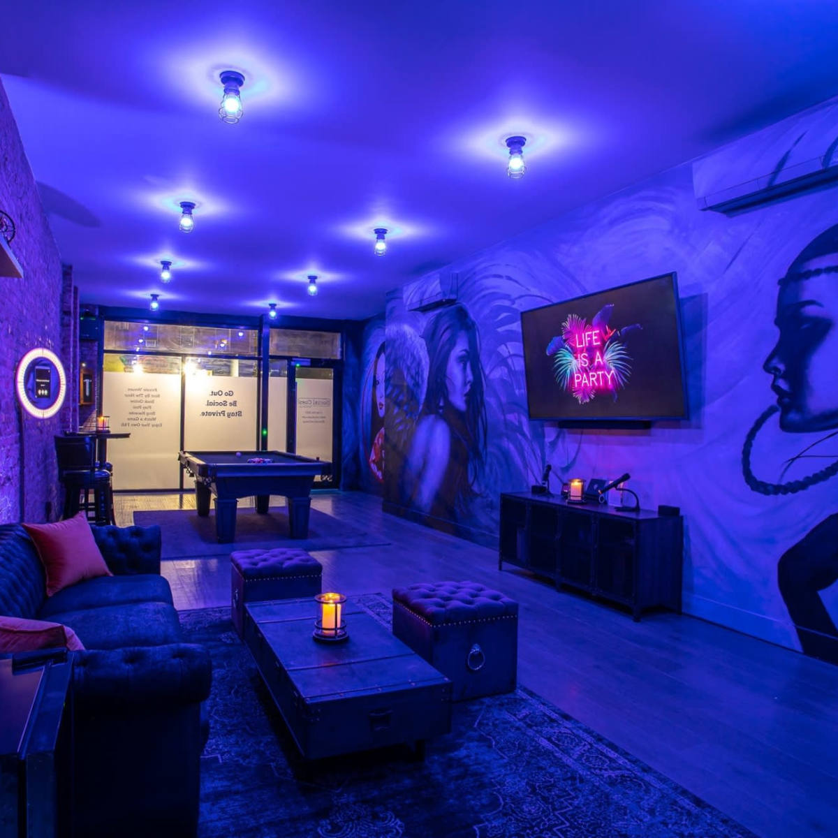 The room features purple lighting, a mural on the wall, a billiards table, and seating with a coffee table, creating a vibrant atmosphere.
