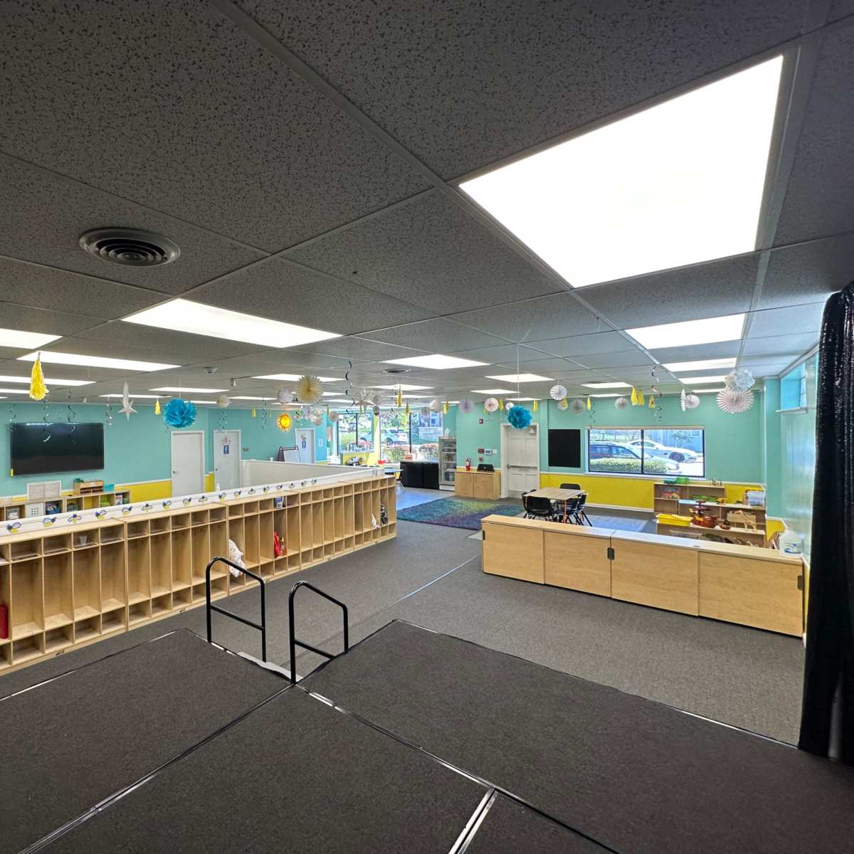 A brightly lit preschool classroom with organized storage shelves and various play areas.